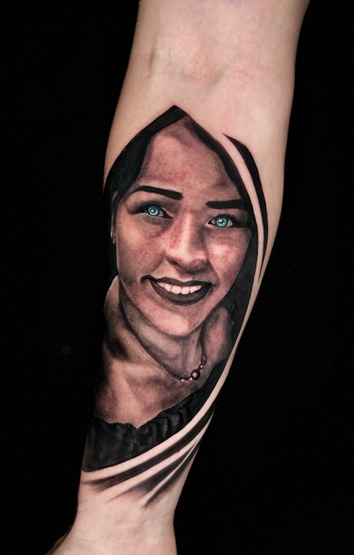 Realistic portrait tattoo of a smiling woman with blue eyes by Ramón Santiago at R INKS ARTS