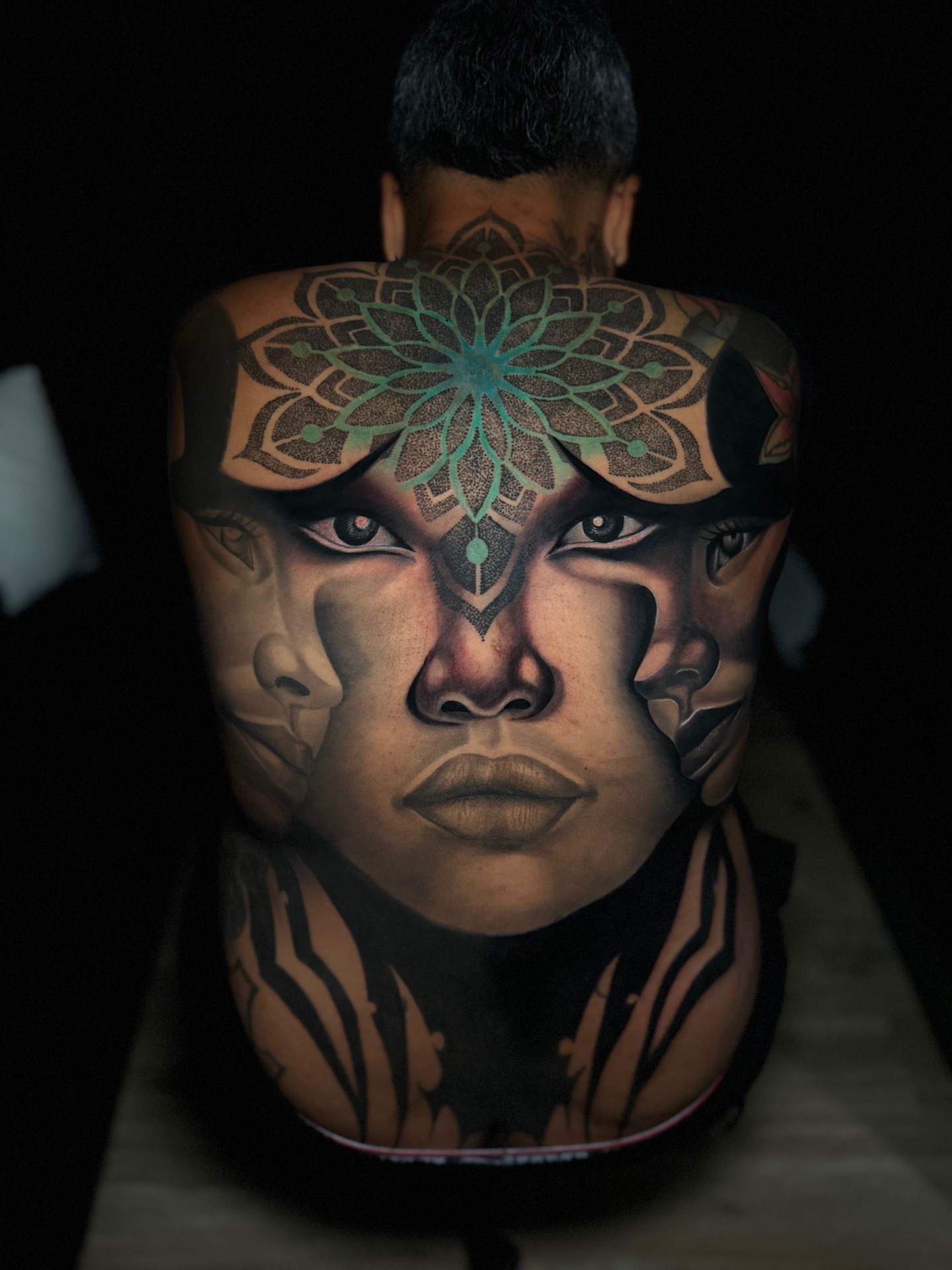 Large-scale back piece with a mandala and surrounded faces by Ramón Santiago at R INKS ARTS