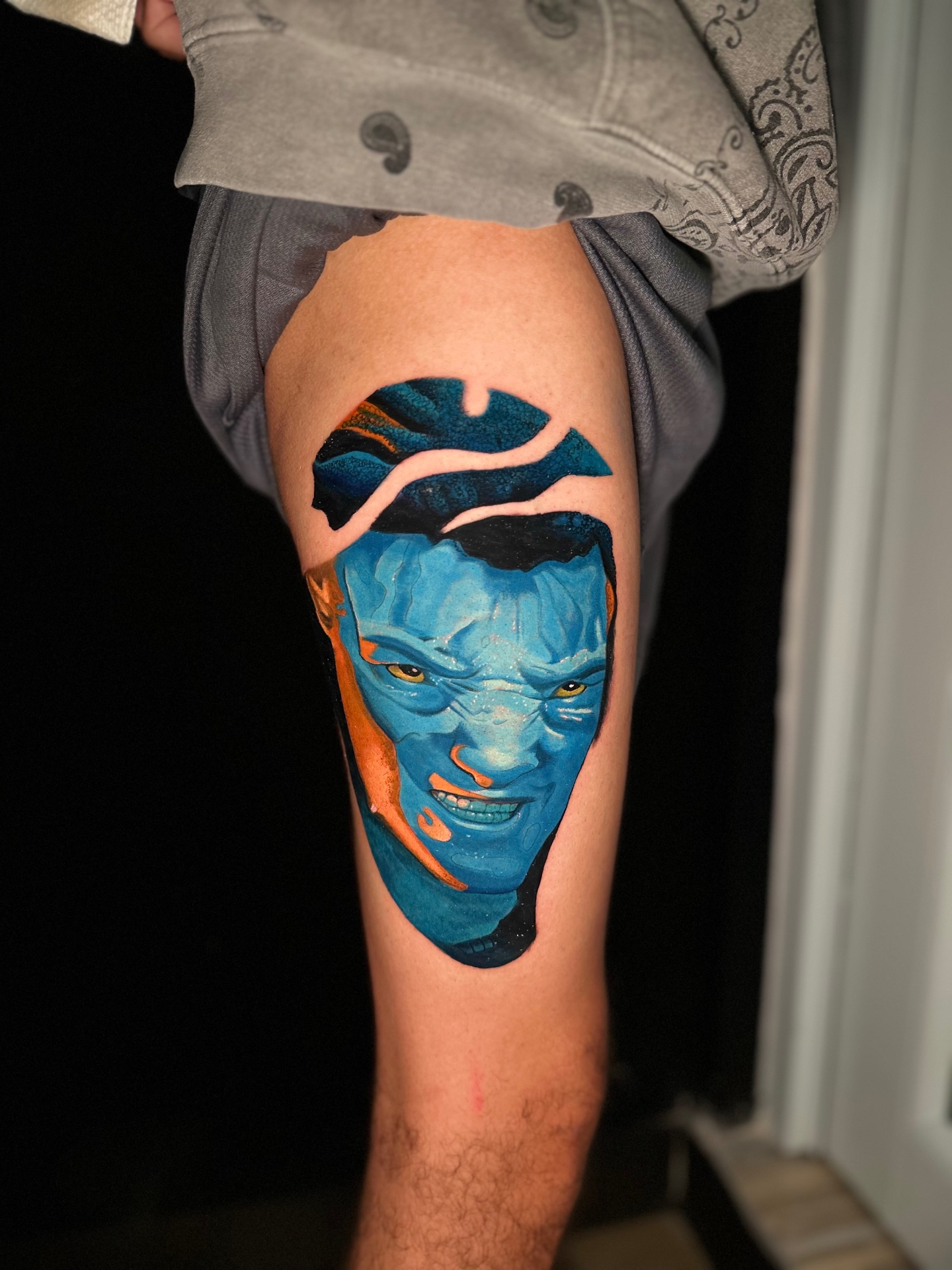 Color realism thigh piece with a blue-toned face in orange and teal by Ramón Santiago at R INKS ARTS